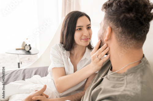 Young woma touching face of her husband in bed