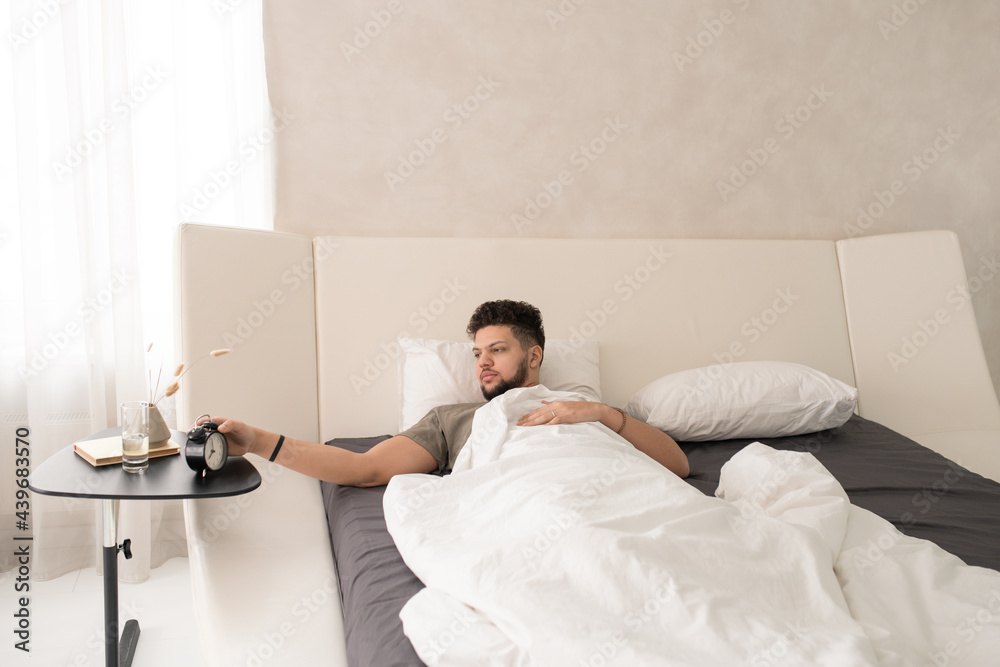 Obraz premium Young man stopping alarm clock in the morning while lying in bed