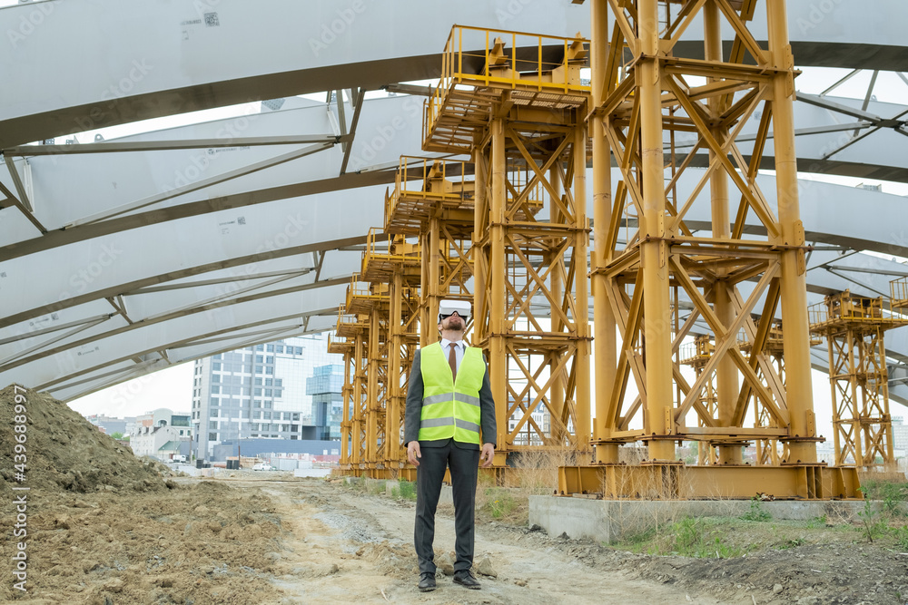 Young builder in formalwear and vr headset standing on construction site