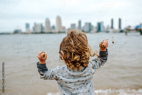 Child throwing handfuls of sand into bay