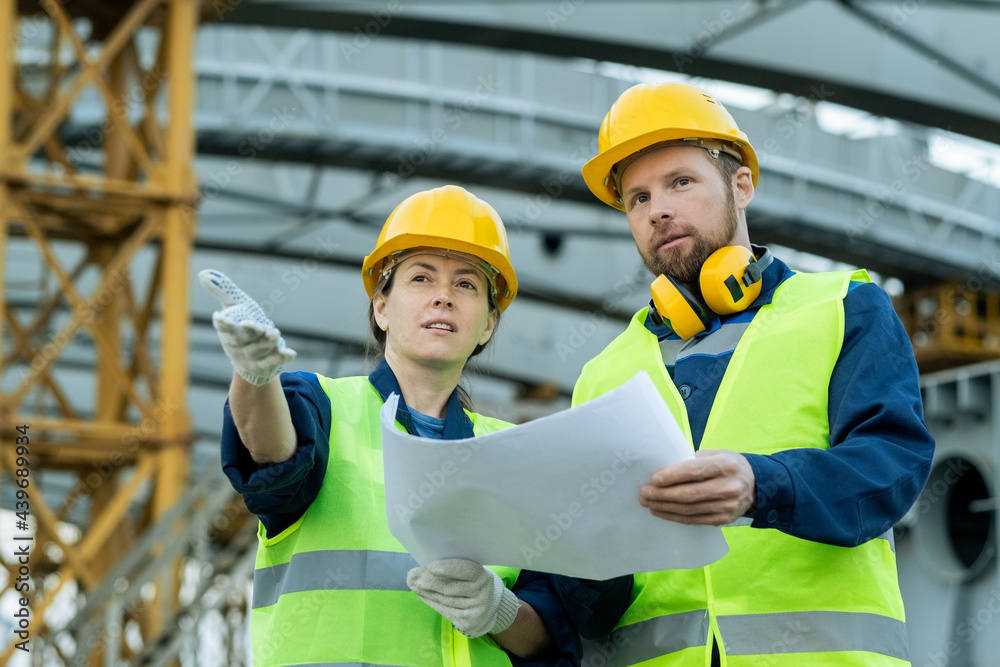 Two confident builders with blueprint discussing construction site Two confident builders with blueprint discussing construction site