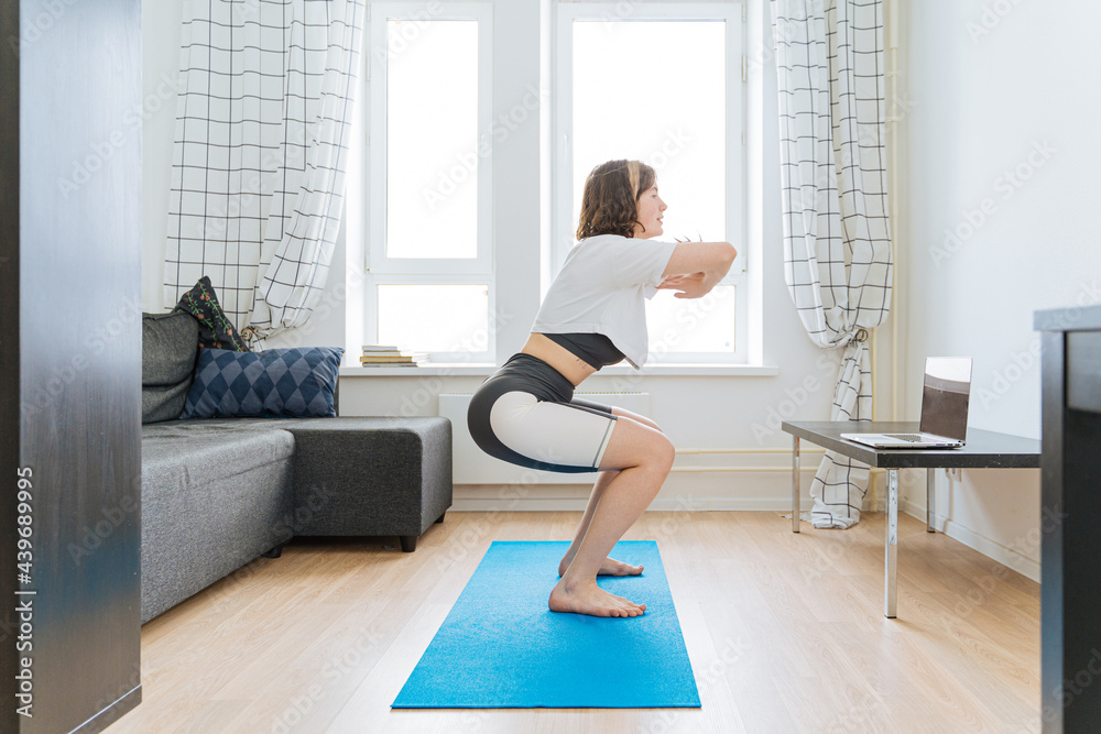 woman doing squats in front of laptop at home woman doing squats in front of laptop at home