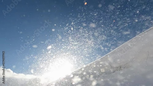 Closeup of snow storm, snow blizzard and snow drift on the mountain slipe during cold winter morning with the sun rays shining through. Slow motion photo