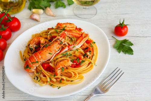 Italian Traditional Dish"Linguine agli Scampi",spaghetti with scampi shrimps,cherry tomatoes,garlics,olive oil,white white,parsley and peppers on plate with white wood table background.Copy space