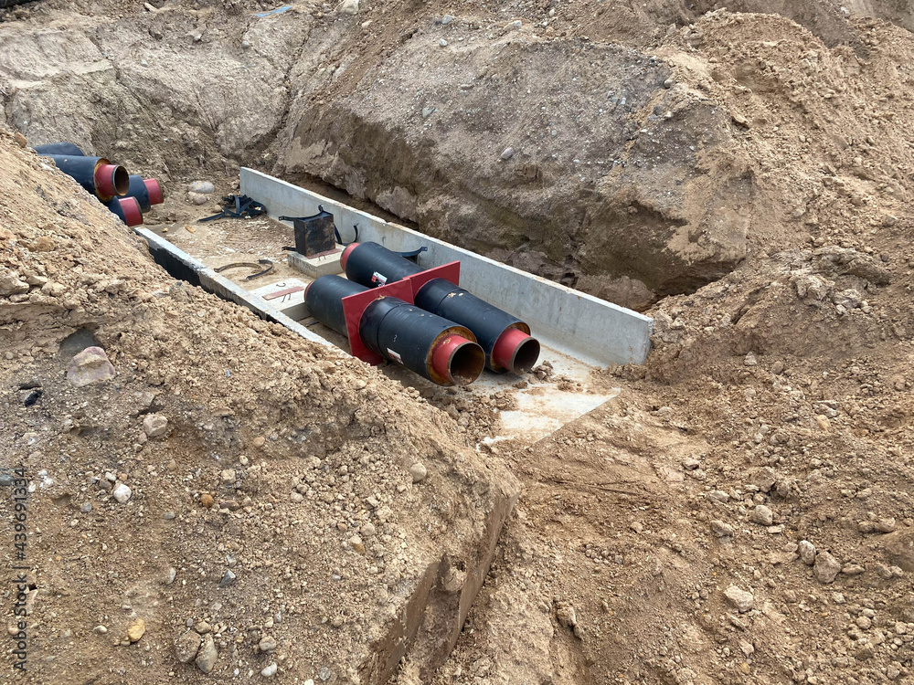 Pipes in trench, industrial pipeline. Insulated pipes to connect a new buildings on heat system. One insulated pipe carries hot water, another carries cool water