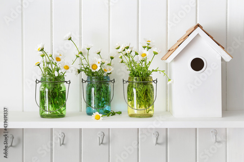 Glass jars of daisies on shelf with birdhouse photo