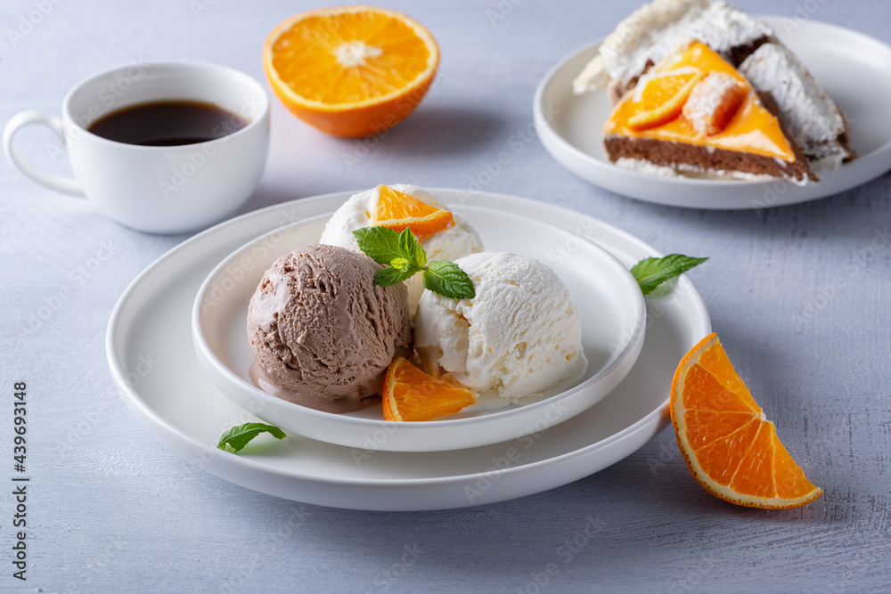 Vanilla and chocolate ice cream, cake and orange slices on a light wooden table