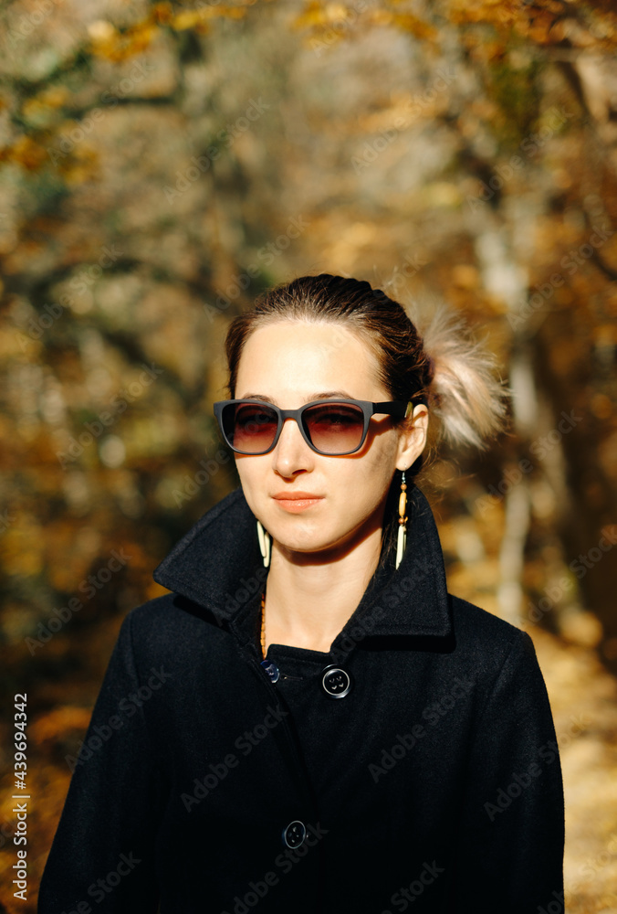 Portrait of a woman who is stylishly dressed in a black coat and sunglasses. Model looks at the camera with restraint. Portrait of a woman who is stylishly dressed in a black coat and sunglasses. Model looks at the camera with restraint.