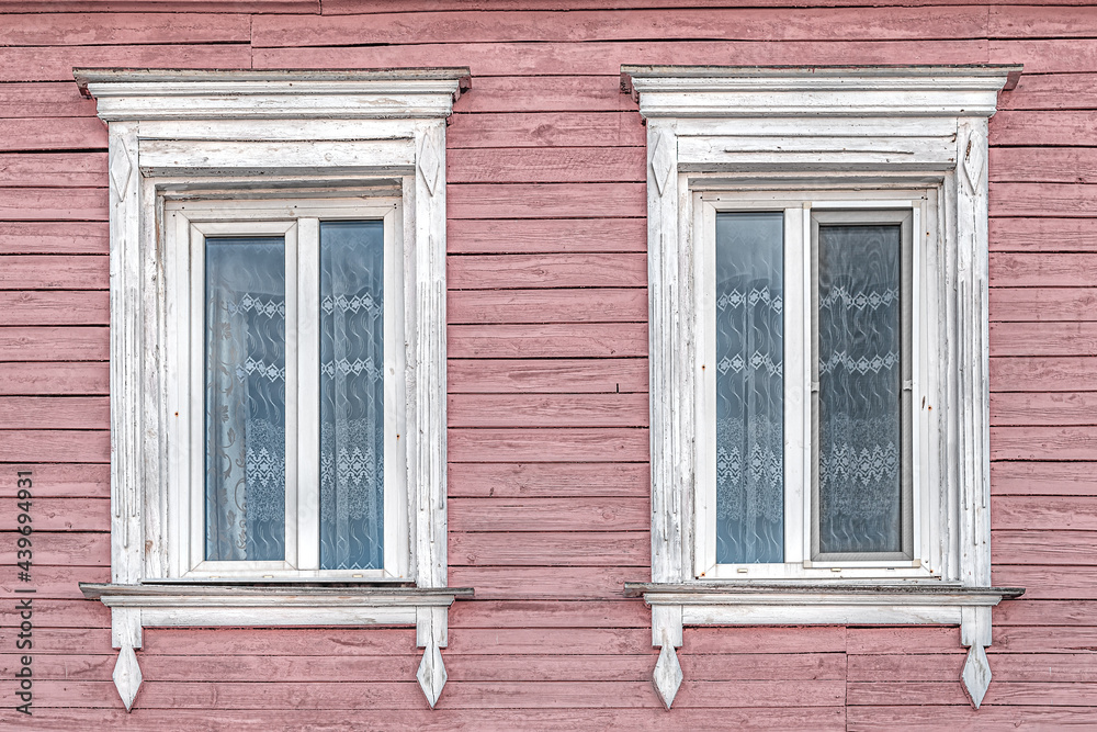 windows with white platbands and vintage curtains in an old wooden painted pink house