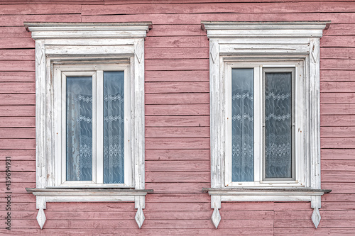 windows with white platbands and vintage curtains in an old wooden painted pink house
