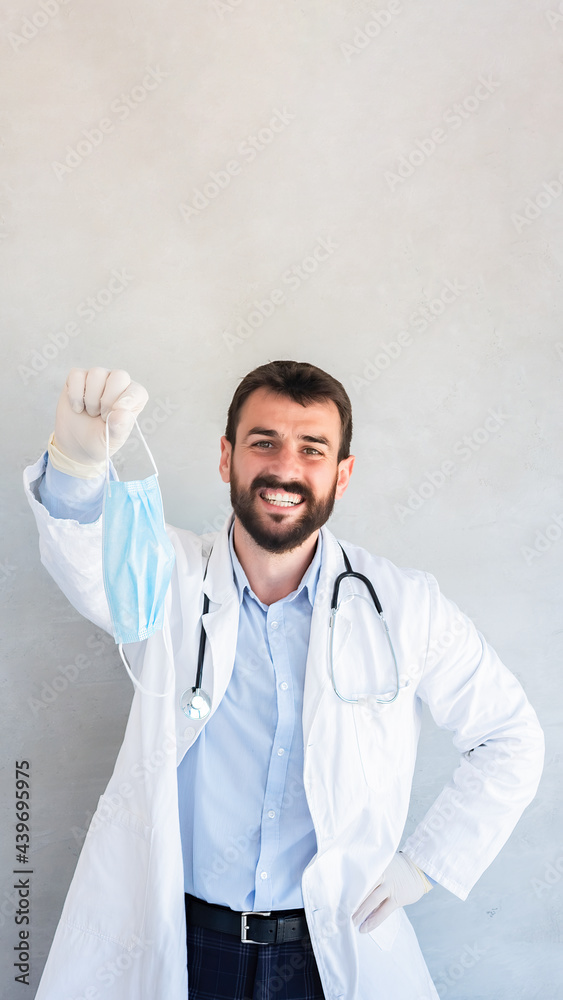 Young smiling doctor showing medical mask, optimistic about pandemic situation.