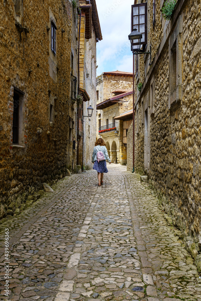 Woman from behind walking through a narrow alley with old stone houses. Santilla del Mar.