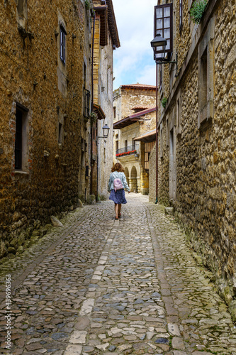Woman from behind walking through a narrow alley with old stone houses. Santilla del Mar.