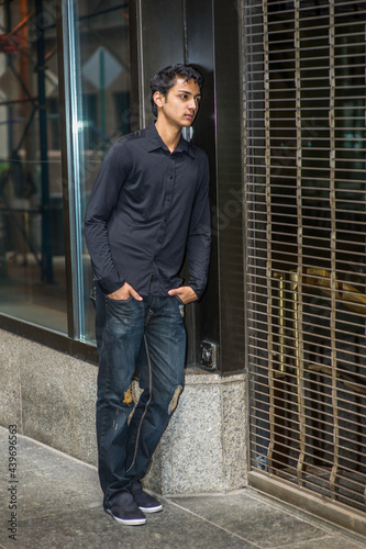 Obraz na płótnie Dressing in a black shirt and a fashionable pants, a young asian teenager is leaning on a closed door, looking inside and thinking. w salonie