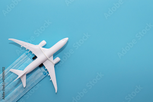 Plane model and medical mask on a blue background with copy space. Safe travels concept. Safety flight and travel during quarantine and lockdown © spyrakot