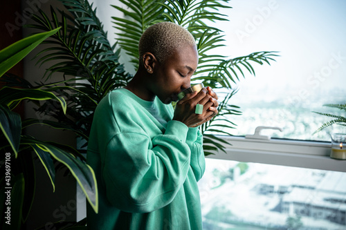 Young African woman drinking tea next to the window.