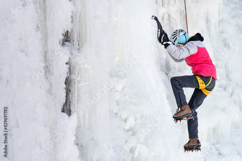 Teen Girl Ice Climbing a Frozen Cliff beside Waterfall in Winter photo