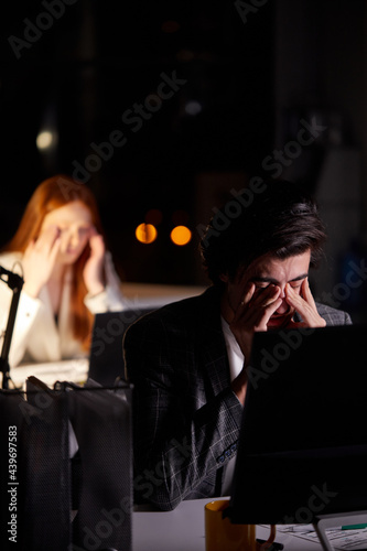 Sleepy exhausted young caucasian man working late night at office desk with pc computer, eyes are gonna closing and man is about to fall asleep, sleep deprivation and overtime overload working concept
