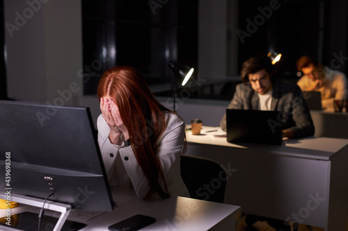 Sleepy redhead business woman working in office at night, sit at desk tired and exhausted, closing face with hands, need some rest, but woman in formal wear miss the deadline at work