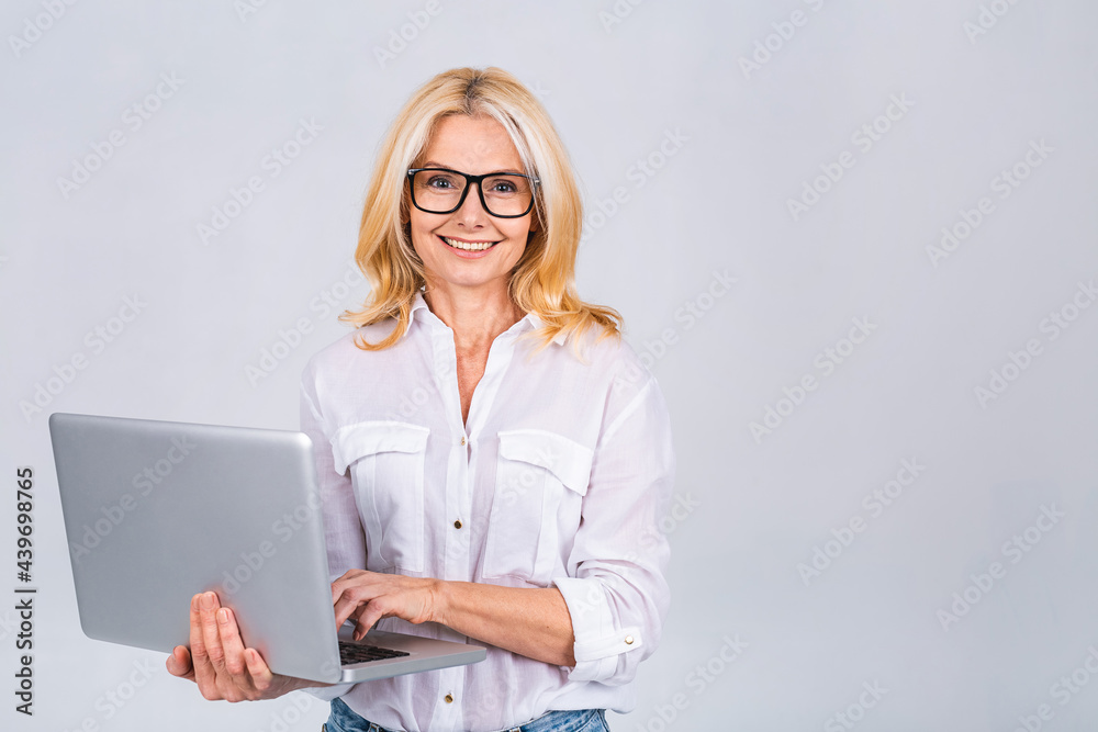 Image of cheerful mature business woman standing isolated over white background using laptop computer. Portrait of a smiling senior lady holding laptop computer. Image of cheerful mature business woman standing isolated over white background using laptop computer. Portrait of a smiling senior lady holding laptop computer.