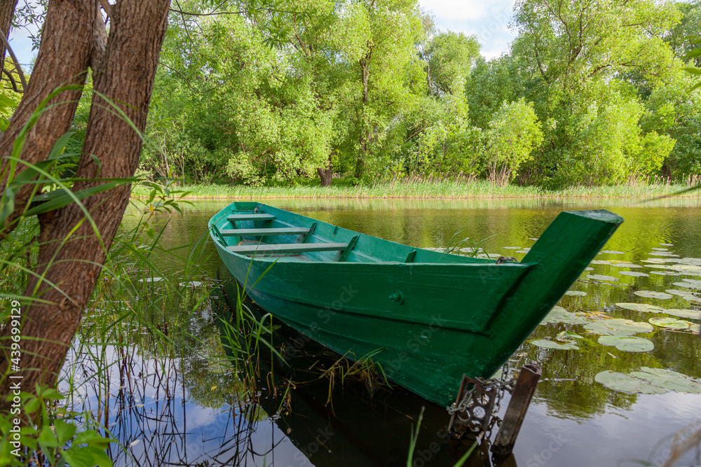 Old green wooden boat tied with a chain near the shore