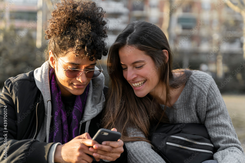 Two young woman smiling and checking their smartphones. Two young woman smiling and checking their smartphones.