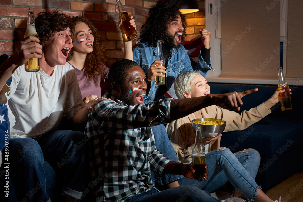 Group of friends watching sport competition on TV together, yelling and screaming by happiness, cheering at home in dark room at night