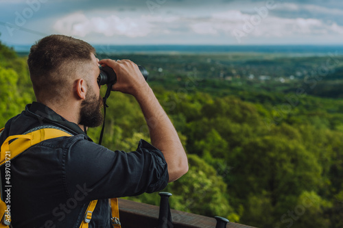 Young hiker man using binoculars while standing on a lookout