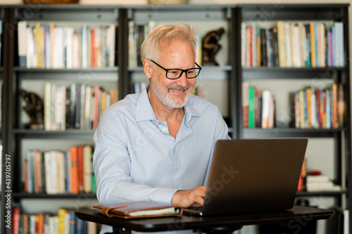 Older Man Laughs While Working on His Laptop at Home  photo