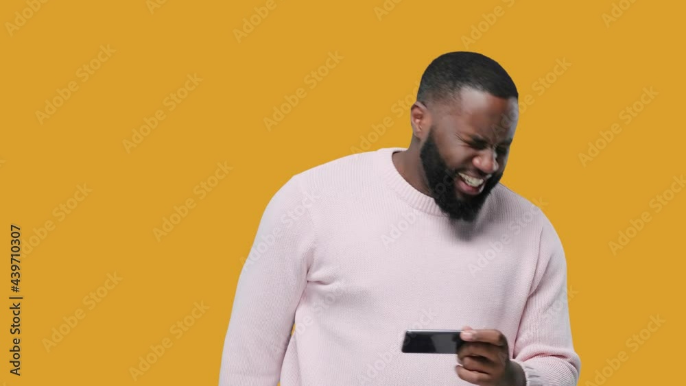 black young man playing game on smartphone on yellow background black young man playing game on smartphone on yellow background