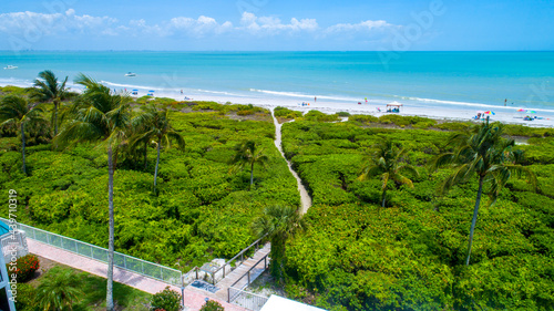 Beach in Sanibel Island, Florida with a wooden walkway going through dense vegetation to the sand photo
