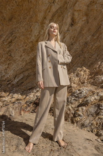 stylish female model standing on beach near rocky cliff photo