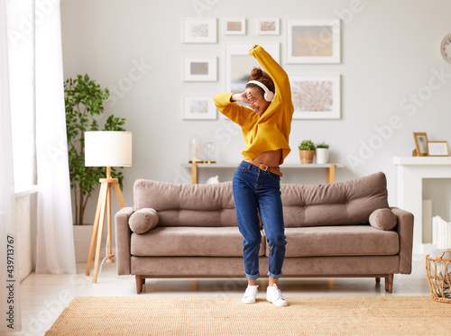 Obraz na płótnie Young playful african american woman in headphones jumping and dancing in living