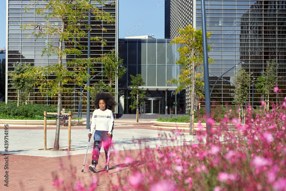 Black woman with crutches walking in city