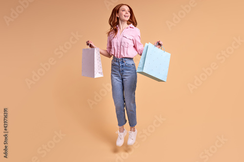 Enjoying of purchasing. Happy excited stylish lady go home after successful shopping holding many packs. Isolated on beige yellow studio background with copy space