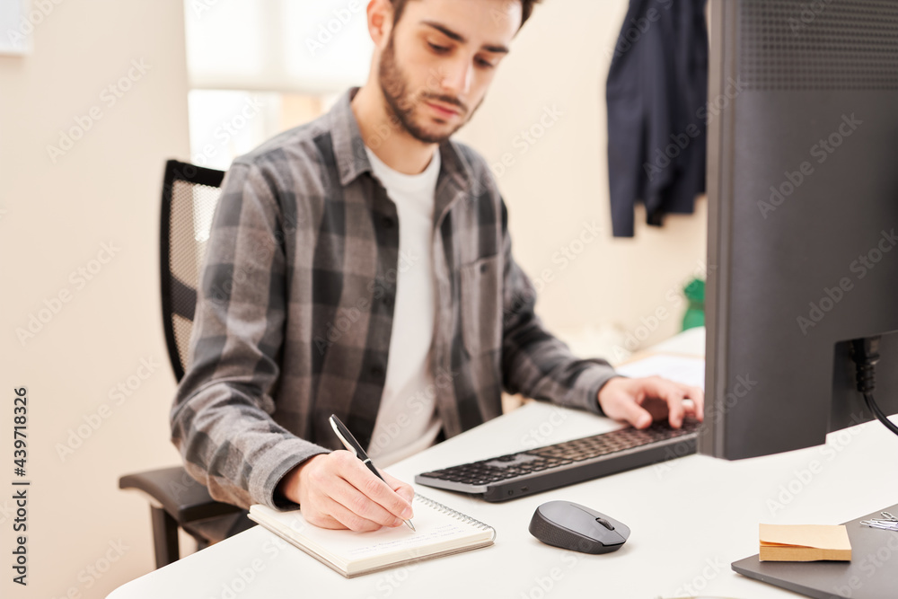 Young man using computer and making notes Young man using computer and making notes