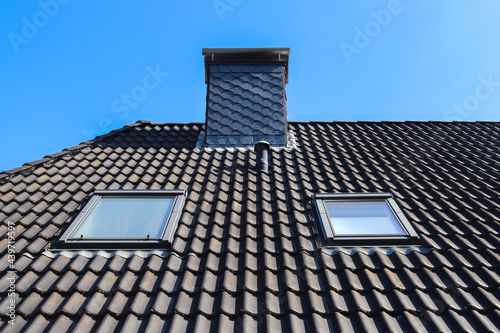 Closeup shot of a roof in Velux style with black tiles on a blue sky background photo