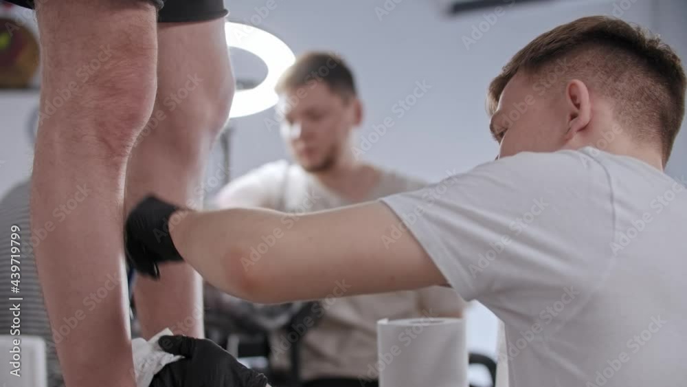 Young man shaves the leg of his client for tattoo in tattoo salon Young man shaves the leg of his client for tattoo in tattoo salon