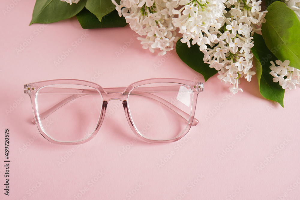 trendy eye glasses and a branch of white lilac on a pink background, eye glasses and flowers