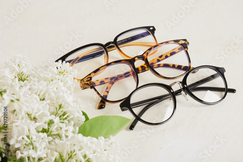 several different trend of eye glasses and a branch of white lilac on a textured beige background, eye glasses and flowers