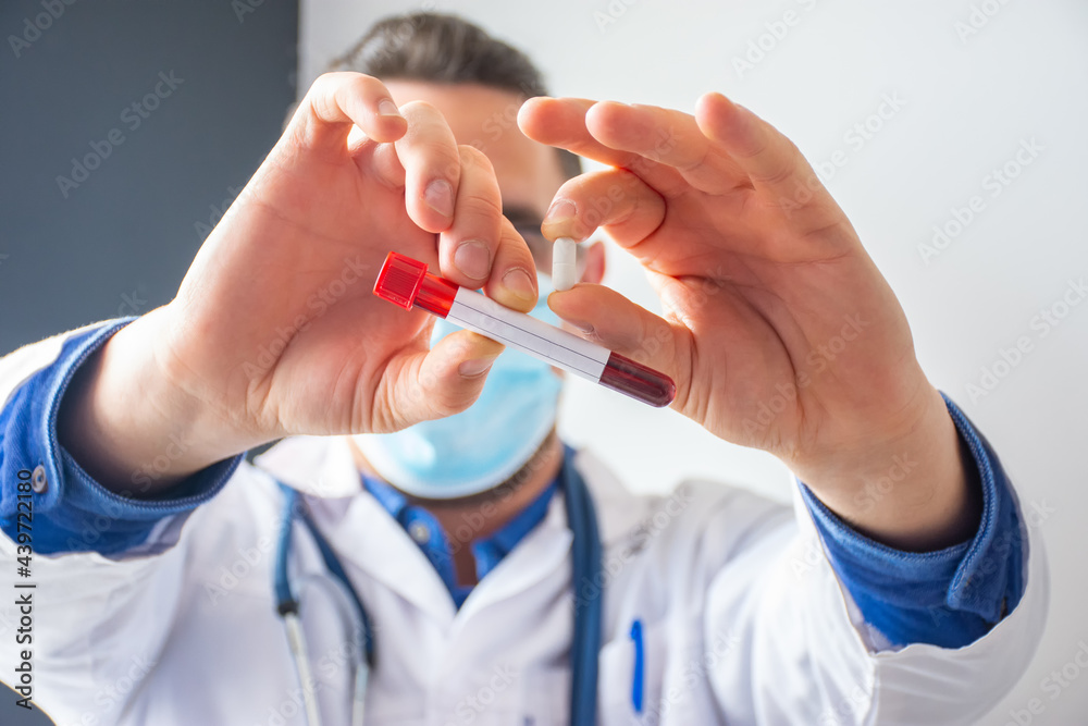 Scientist, doctor or medical professional holds in his hand laboratory test tube with blood and indicated positive result, in another pill as medicine for treatment of coronavirus Scientist, doctor or medical professional holds in his hand laboratory test tube with blood and indicated positive result, in another pill as medicine for treatment of coronavirus