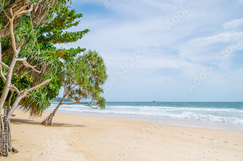 Empty tropical summer beach background Green trees leaves frame with blue sky and white sand beach Wave crashing on sandy shore Amazing beach at Phuket Thailand.