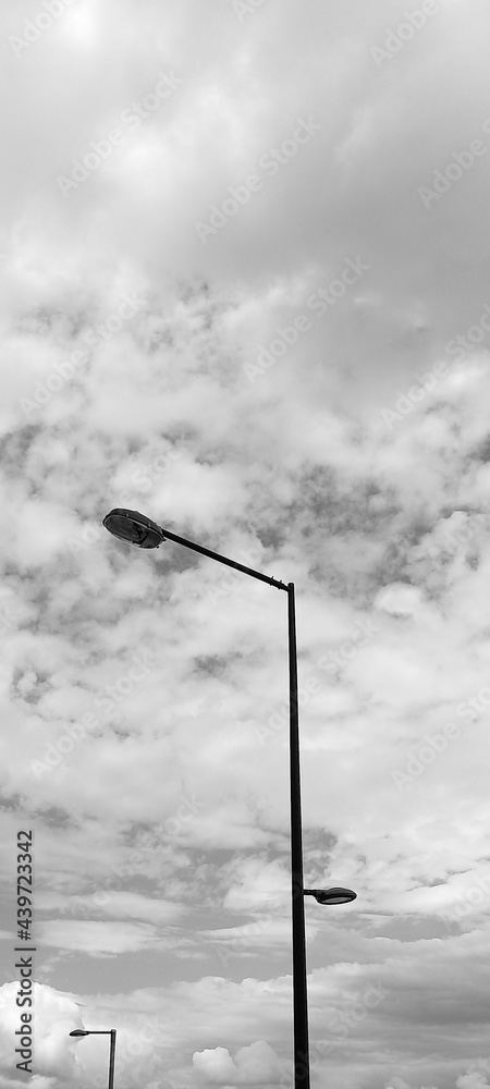 Minimalist photo composed by a lamppost, with clouds of a cloudy day in the background. In black and white, bringing a sophistication and an air of mystery to the composition.