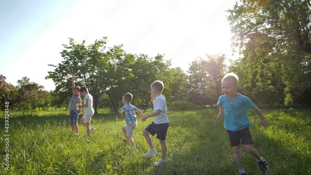 Slow-motion video. A group of children, friends of boys and girls, running merrily in the park on a sunny summer day in casual clothes on a green meadow. The concept of a child's dream. Family games Slow-motion video. A group of children, friends of boys and girls, running merrily in the park on a sunny summer day in casual clothes on a green meadow. The concept of a child's dream. Family games