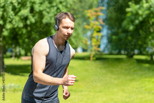 sporty young male athlete run and listen music with headphones on nature. guy do sport in the park in city. healthy lifestyle. marathon man runner training. outdoor fitness.