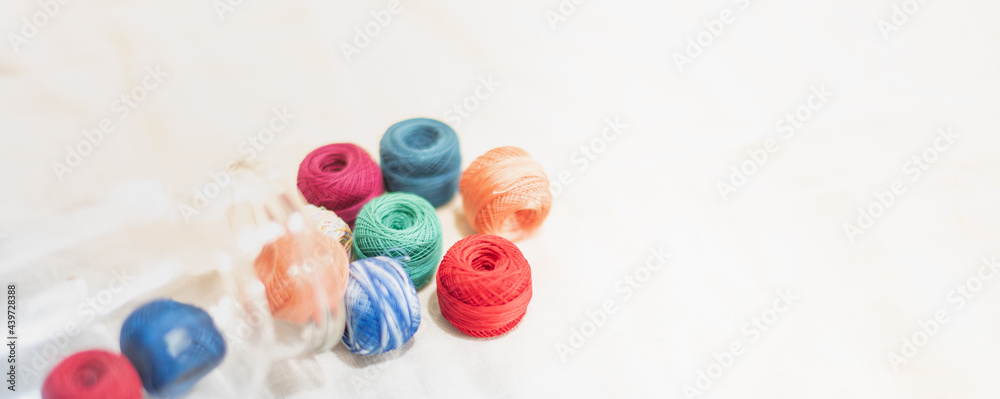 Colored balls of yarn in the glass bottle and put on the white cotton background Colored balls of yarn in the glass bottle and put on the white cotton background