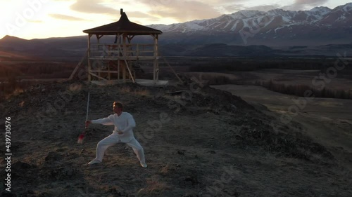 Video of kungfu master in a white sports uniform training wushu with jian sword on the hill. photo