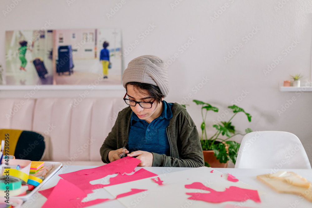 Boy cutting figures off paper spending time at home Boy cutting figures off paper spending time at home