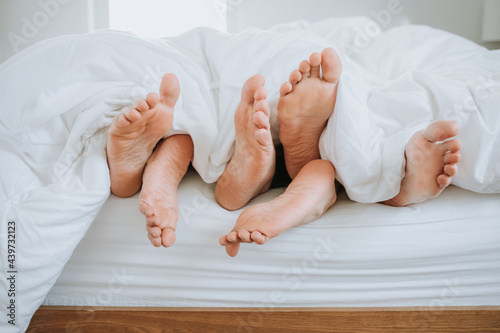 Closeup of Three Pairs of Feet in Bed photo