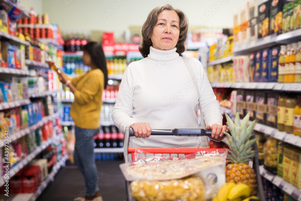 Portrait of positive interested elderly woman visiting supermarket food department for shopping
